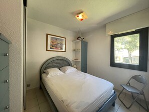 A bedroom with a bed, a chair, a window, a painting, and a cabinet.