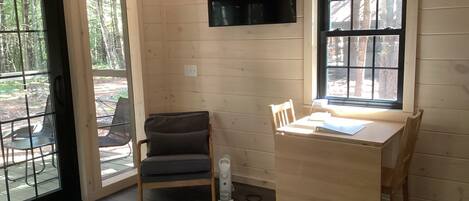 Una habitación con interior de madera, una mesa con sillas, un televisor montado en la pared y una ventana con vistas a árboles.