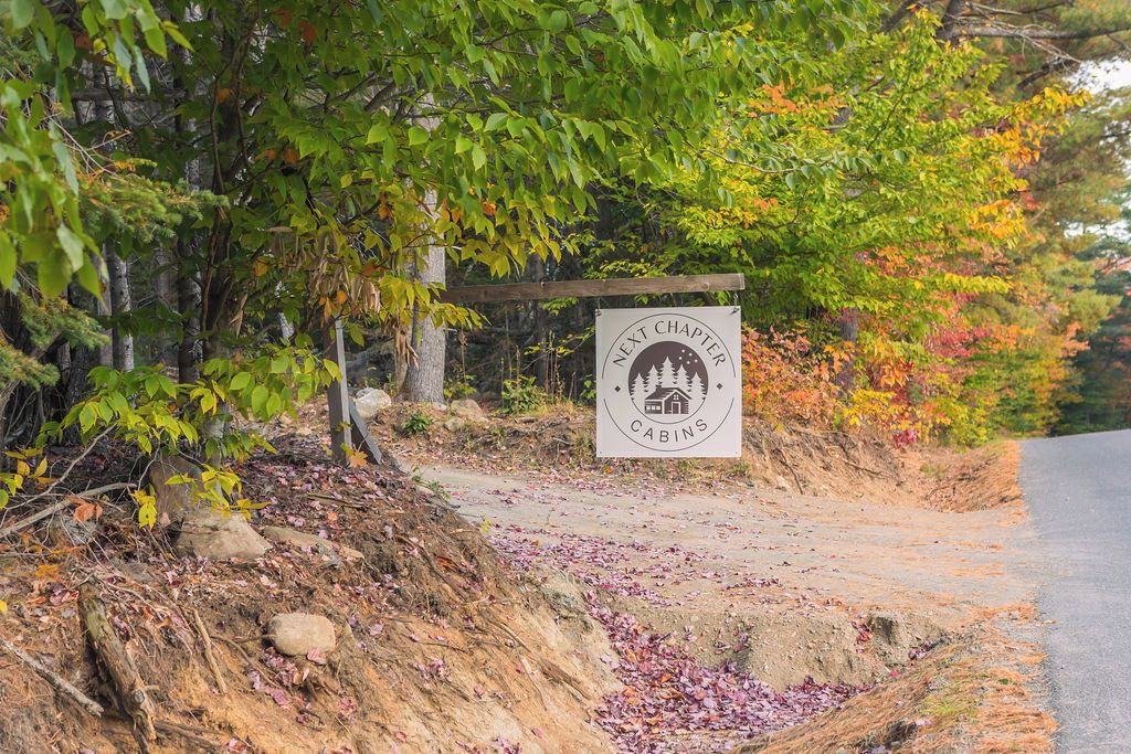 A sign for 'Next Chapter Cabins' with a rustic wooden fence and trees in the background.