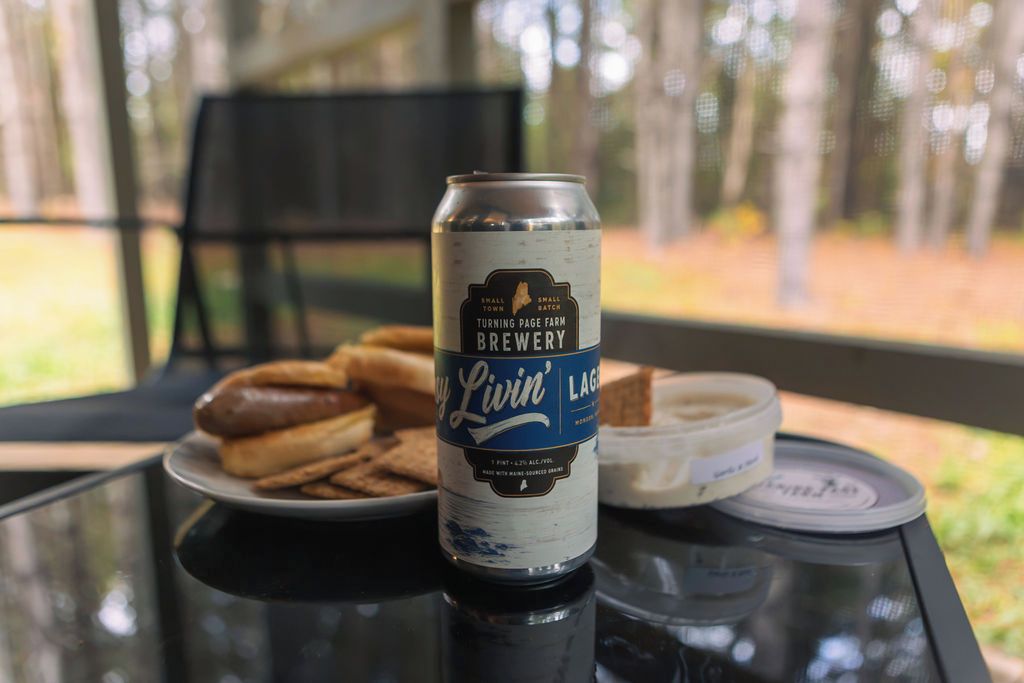 Una lata de cerveza sobre una mesa con un plato de comida y un recipiente con mantequilla.