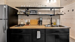 A modern kitchen with a stainless steel refrigerator, a wooden countertop, a gas stove, a coffee maker, and a sink.