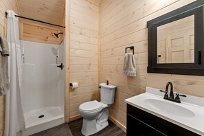 Une salle de bain aux murs lambrissés, équipée d’une douche, de toilettes, d’un lavabo et d ’un miroir.