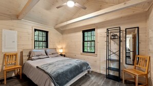 A cozy bedroom with a bed, two chairs, a nightstand, a mirror, and a wardrobe.