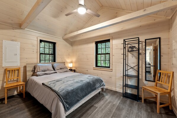 Un dormitorio acogedor con cama, dos sillas, una mesita de noche, un espejo y un armario.