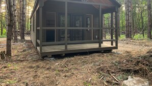 Une petite cabane avec une terrasse en bois, entourée d’une forêt.