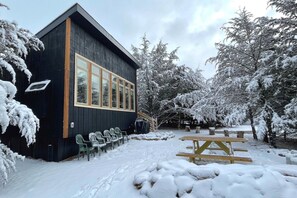 A black building with large windows and a wooden deck with chairs and a picnic table. - Modern Cabin. Communal Sleeping - 2 Queen Beds + Full Trundle (Ashland)