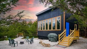 A cabin with a deck, outdoor seating, and a barbecue grill.