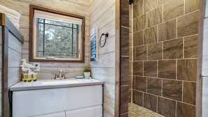 A bathroom with a wooden vanity, a window, and a shower area with dark tiles.