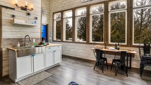 A modern kitchen with a large window, wooden walls, and a dining area with chairs.
