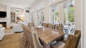 A spacious dining area with a large wooden table and wicker chairs, surrounded by large windows offering views of the outdoors. - Pet Friendly, Lake District Watercolor, Tesla Charger (Santa Rosa Beach)