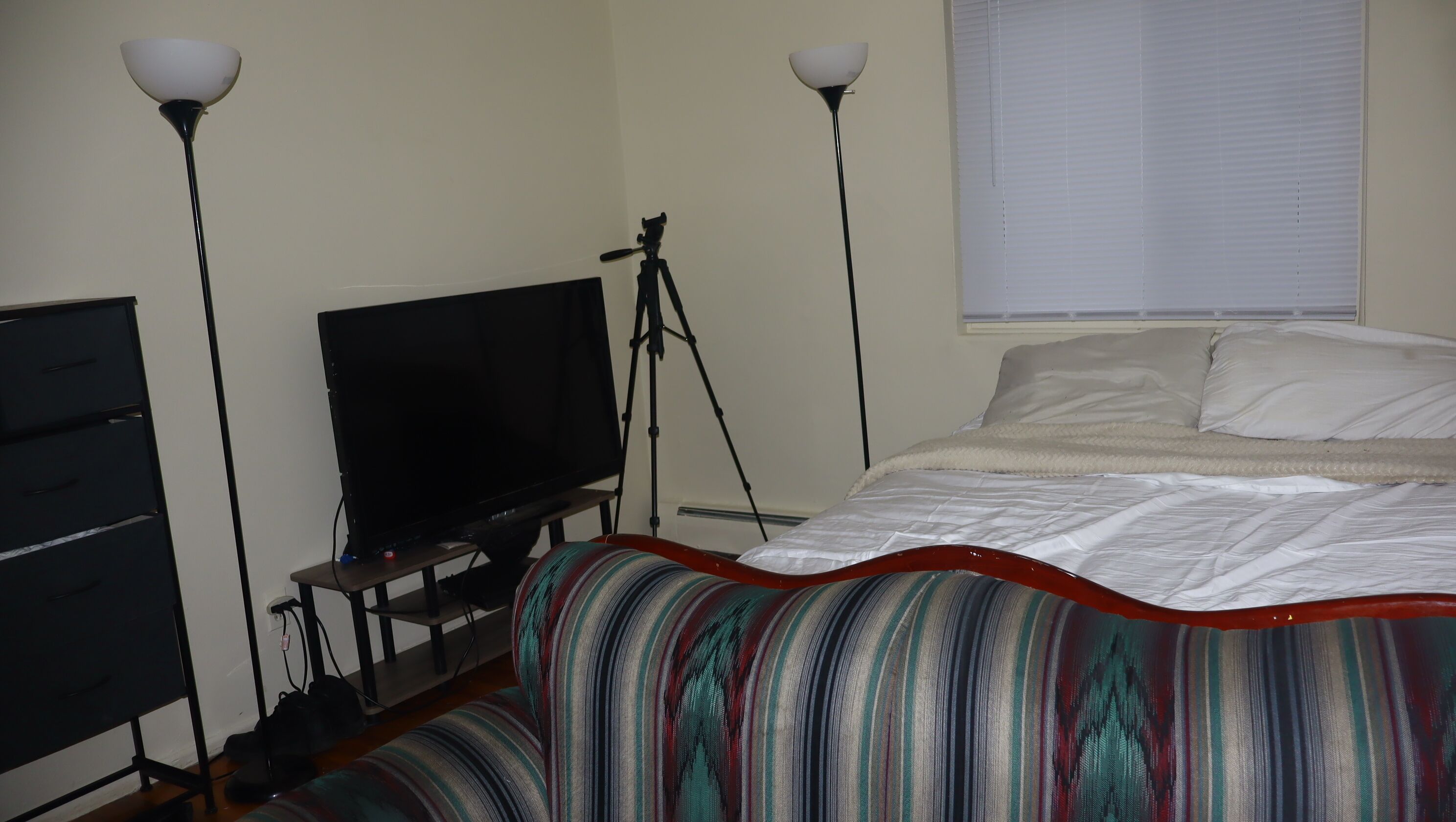 A bedroom with a bed, a television, a desk with a computer, and two standing lamps.