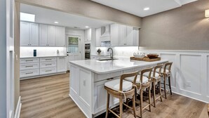 A modern kitchen with white cabinetry, a central island, bar stools, and a view of the adjacent dining area. - 6 Wood Duck Court at The Sea Pines Resort (Hilton Head Island)