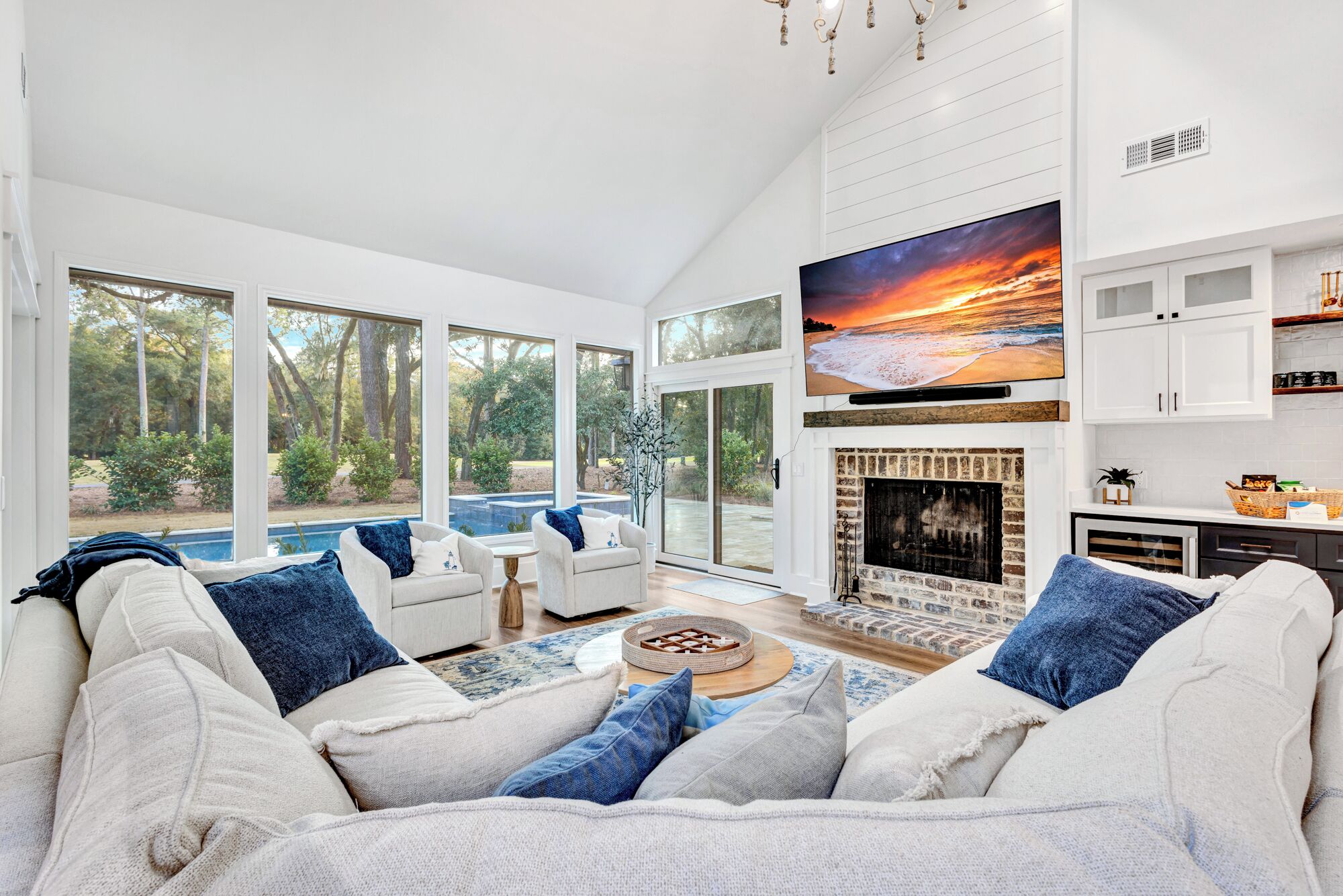 A spacious living room with a large TV, a fireplace, and a view of a swimming pool and trees.
