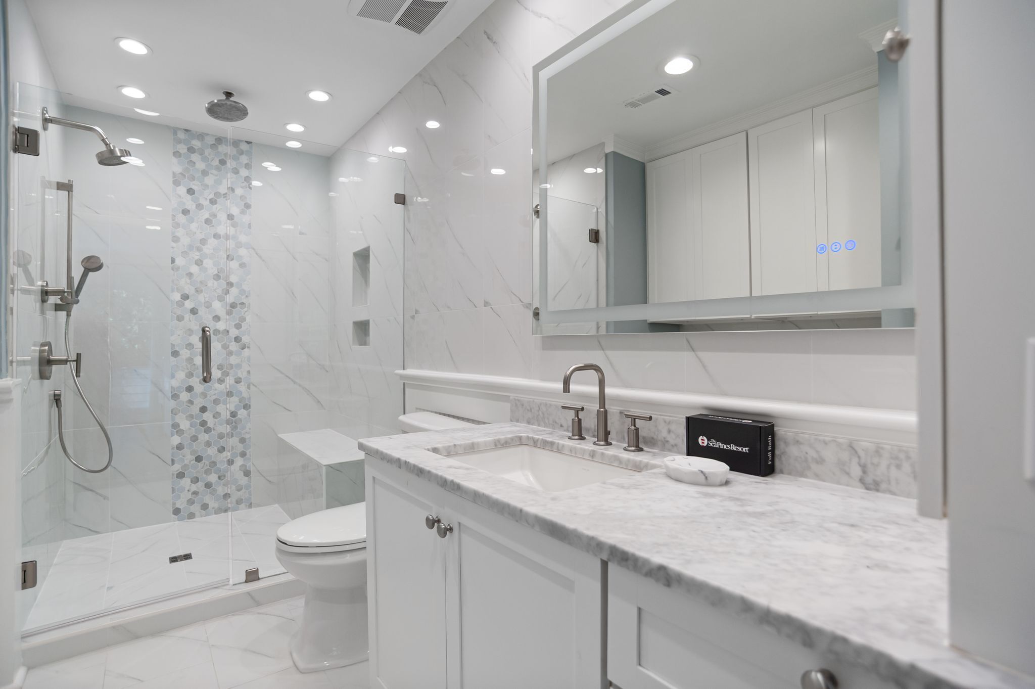 A modern bathroom with a glass-enclosed shower, a white toilet, a marble countertop, and a large mirror above the sink.