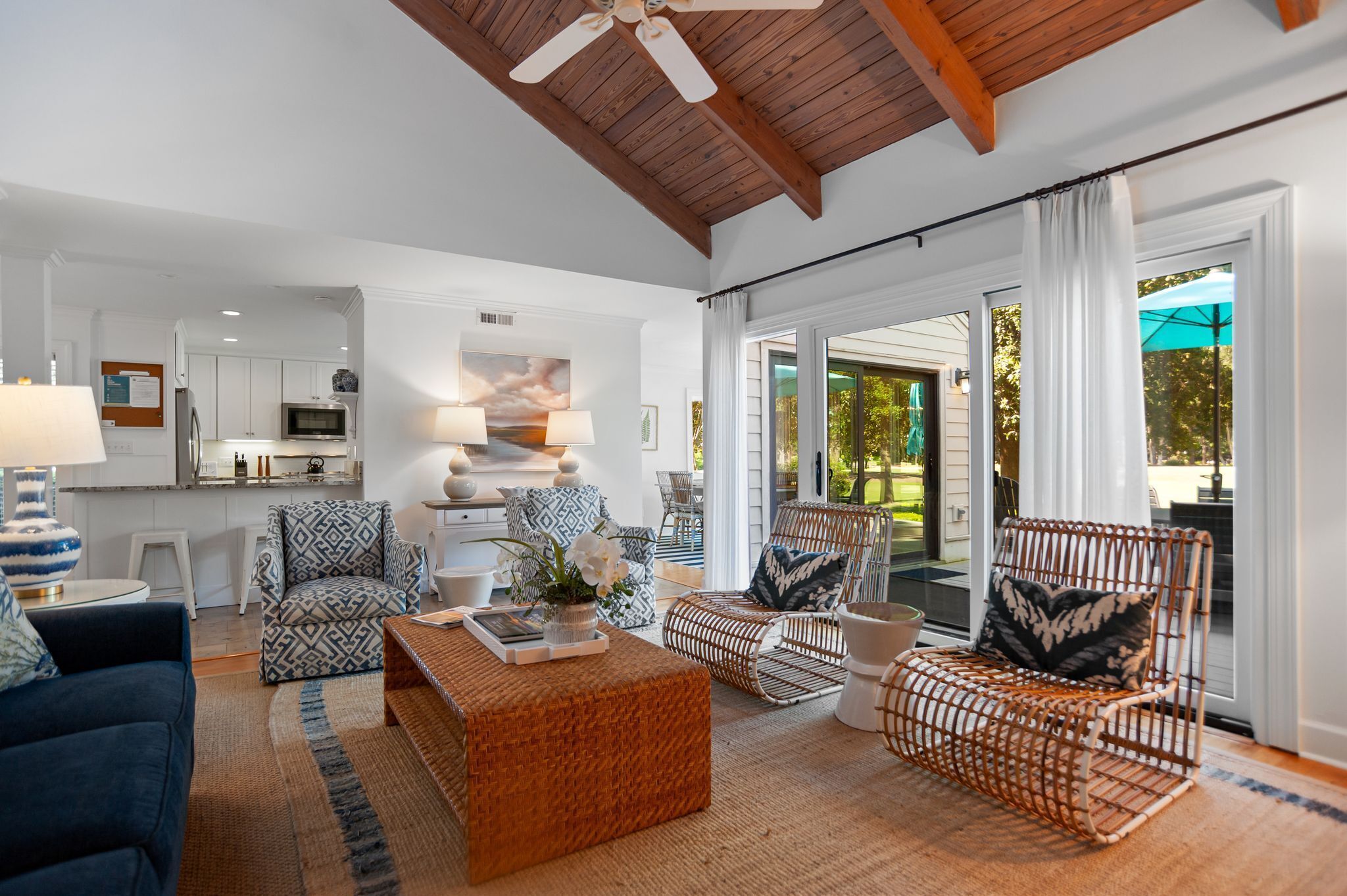 A spacious living room with a high ceiling, wicker furniture, and a view of the outdoors.