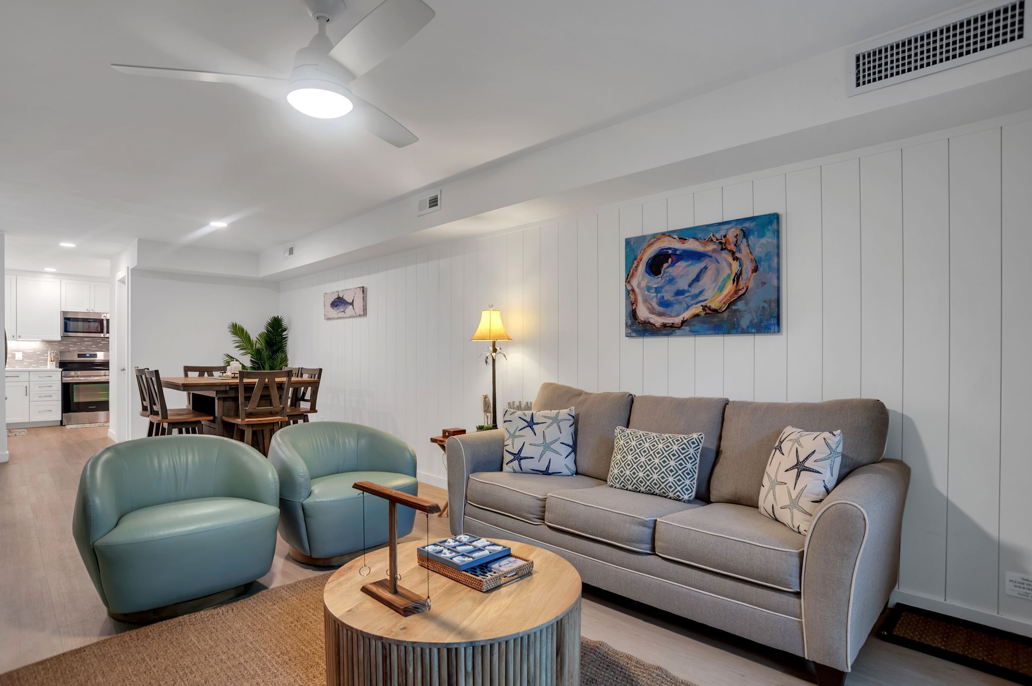 A modern living room with a grey sofa, two blue armchairs, a wooden coffee table, and a painting on the wall.