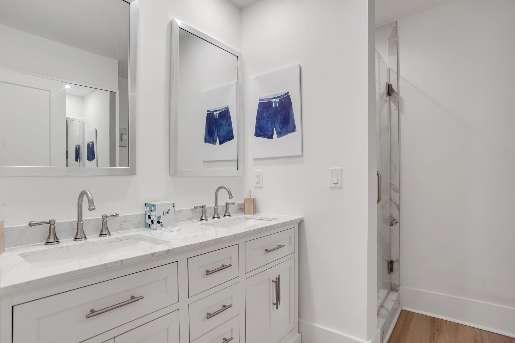 A modern bathroom with a double sink vanity, a large mirror, and a shower area.