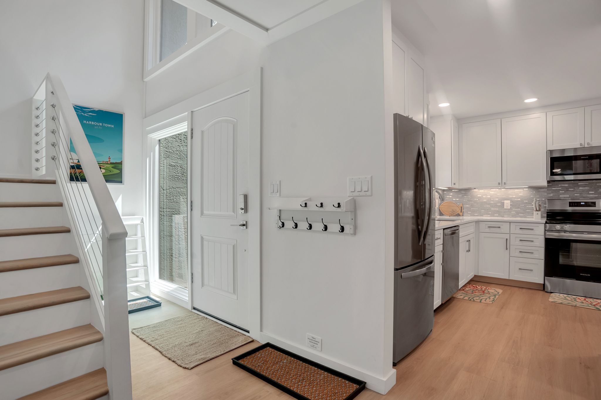 Une cuisine moderne avec des meubles blancs, des appareils électroménagers en acier inoxydable et un escalier en bois.