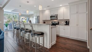 A modern kitchen with white cabinetry, stainless steel appliances, and a central island with bar stools. - 1266 Harbour Town Club at The Sea Pines Resort (Hilton Head Island)