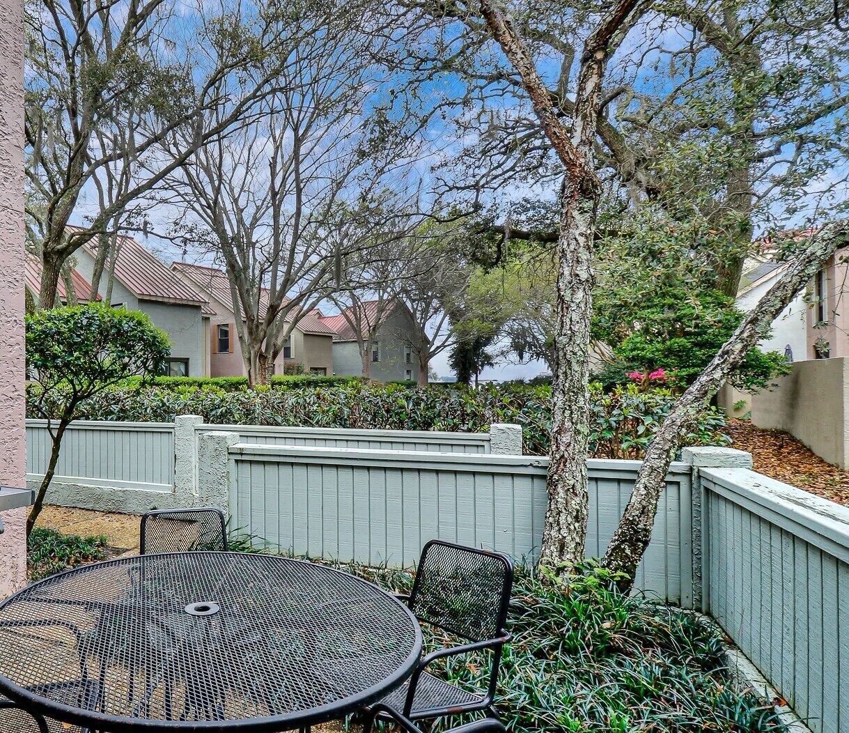 A patio with a round metal table and chairs, surrounded by a low fence and various plants.
