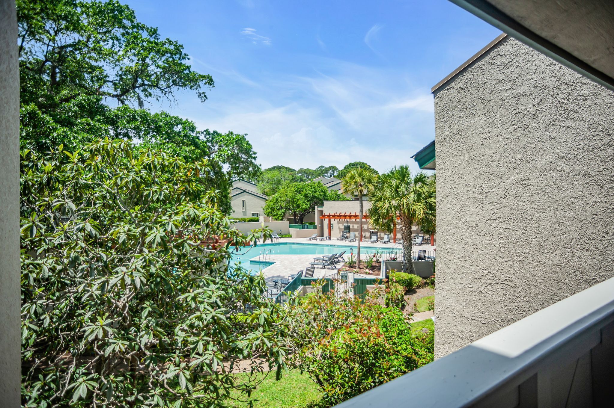 A view of a swimming pool with lounge chairs, surrounded by greenery and buildings.