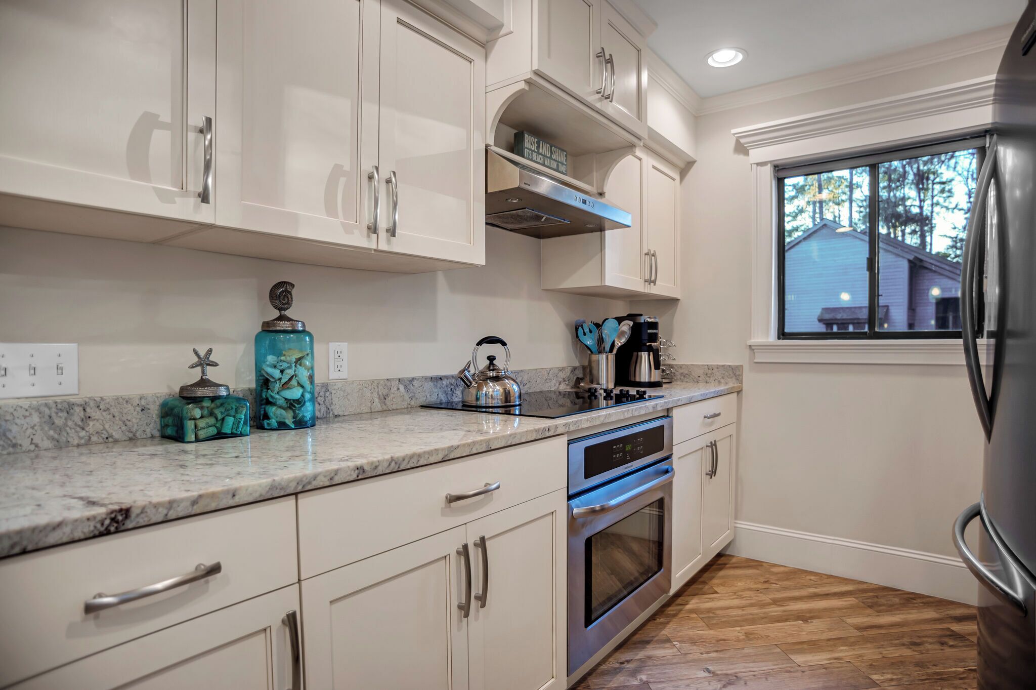 Cocina moderna con armarios blancos, un refrigerador de acero inoxidable y una ventana con vista a una casa.