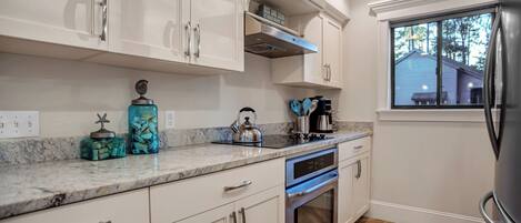 Cocina moderna con armarios blancos, un refrigerador de acero inoxidable y una ventana con vista a una casa.
