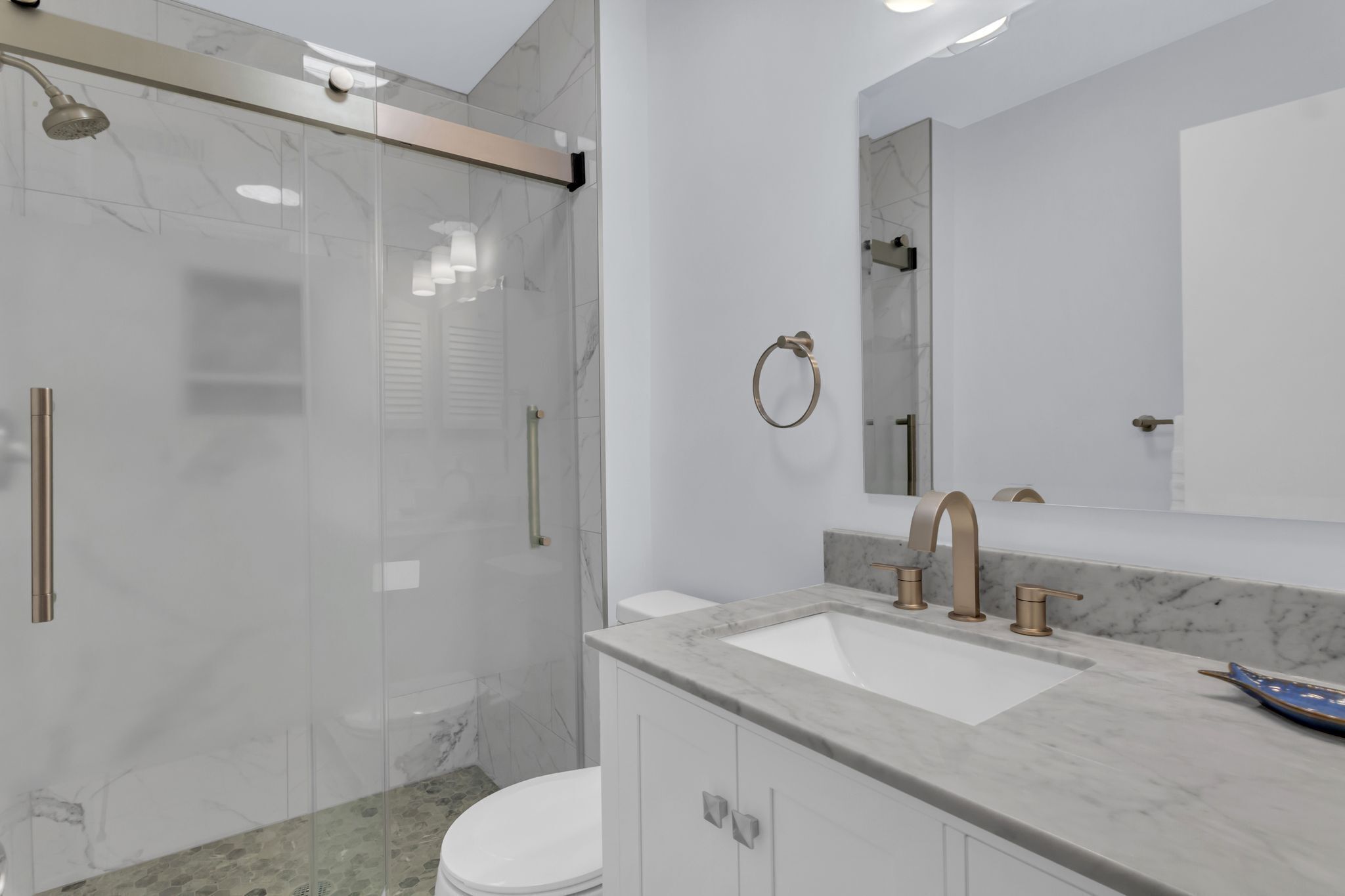 Un bagno moderno con doccia vetrata, un WC bianco, un lavabo in marmo e uno specchio grande.