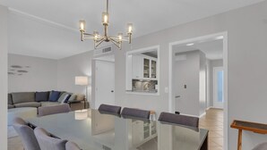 A modern dining area with a glass table, grey upholstered chairs, and a chandelier.
