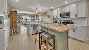 A modern kitchen with white cabinetry, a large island with stools, and a view to the outdoors. - 1852 Beachside Tennis at The Sea Pines Resort (Hilton Head Island)