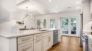 Una cocina moderna con armarios blancos, encimera de mármol, electrodomésticos de acero inoxidable y una isla grande con pileta.