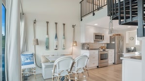 A modern kitchen with white cabinets, stainless steel appliances, and a dining area with wicker chairs.