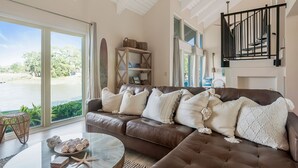 A spacious living room with a leather sofa, a glass coffee table, and a view of a lake.