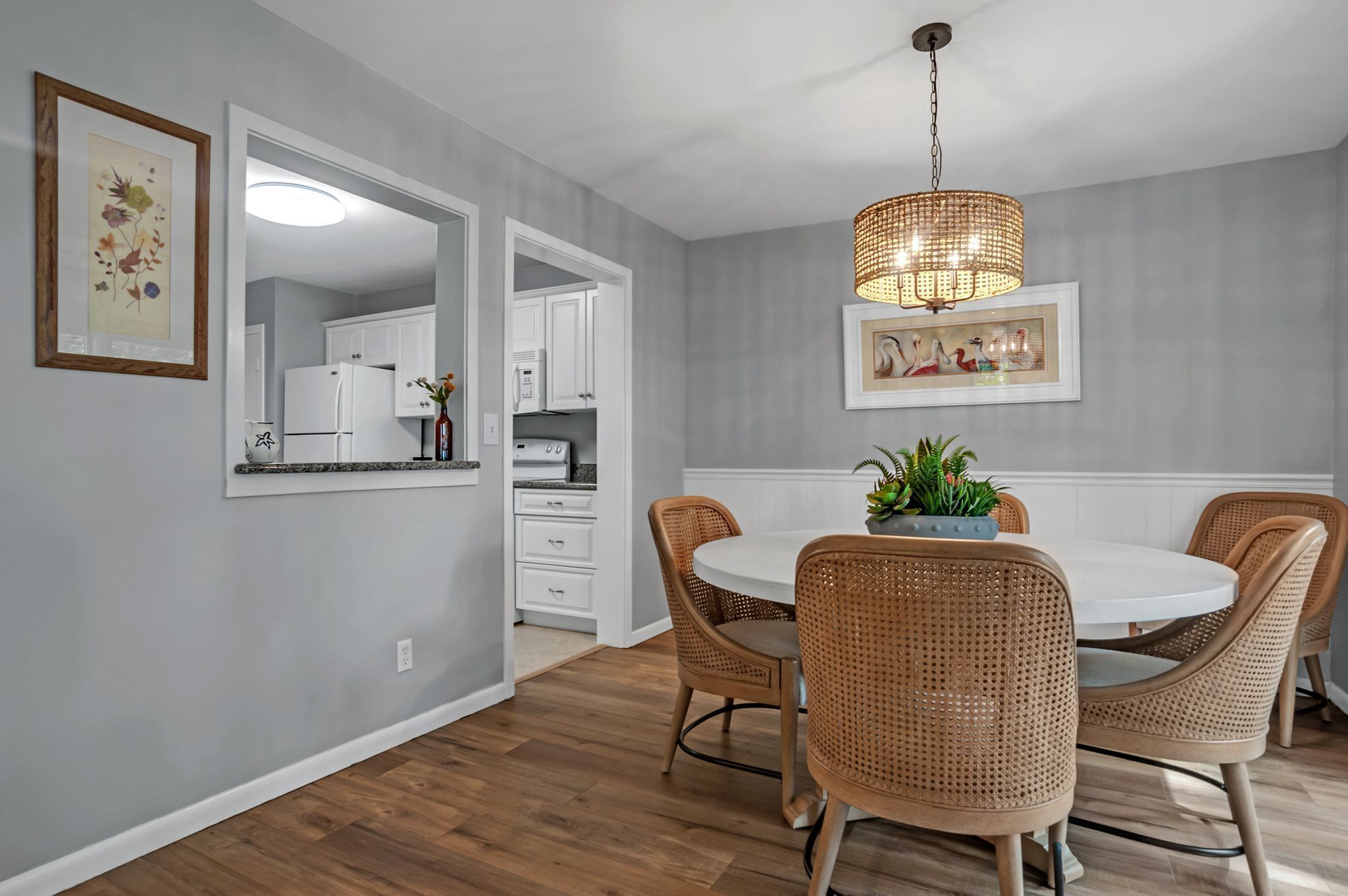 A modern kitchen with white cabinets, a dining area with wicker chairs, and a hanging light fixture.