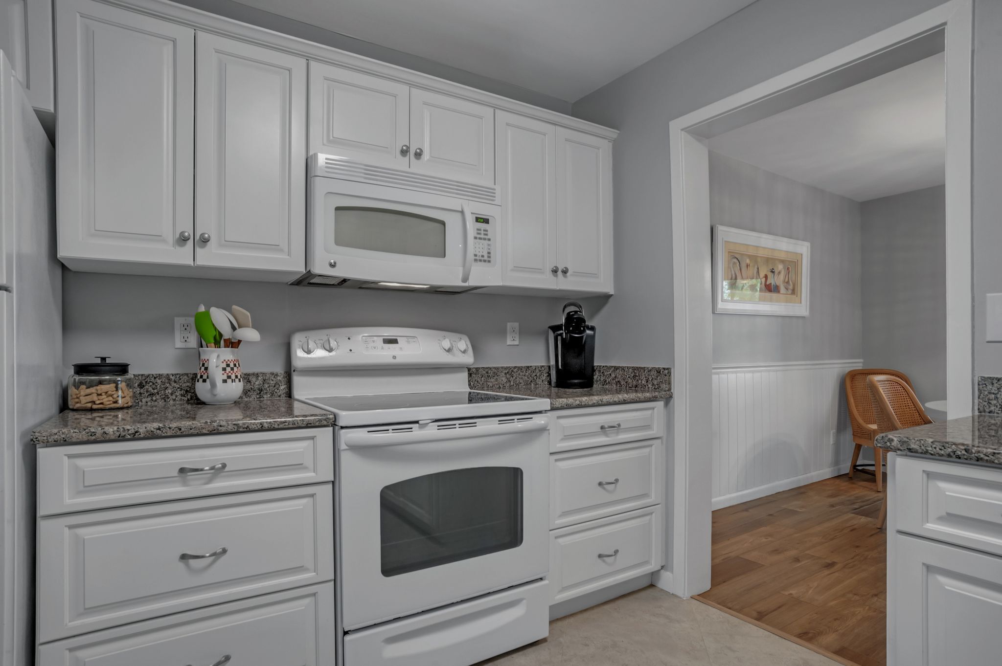 A kitchen with white cabinets, a microwave, stove, and a coffee maker.