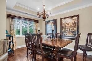 A dining room with a wooden table, chairs, a chandelier, and large framed artwork on the walls. - 1112 Harbour South Club Villa at The Sea Pines Resort (Hilton Head Island)