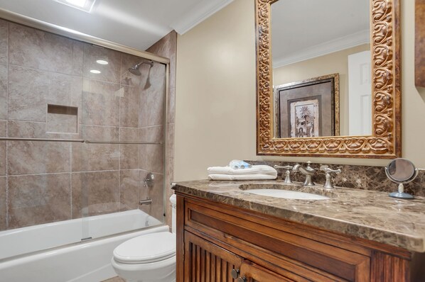 A bathroom with a bathtub, toilet, vanity with a sink, and a large mirror.