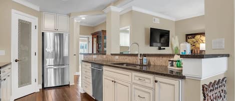 A modern kitchen with a stainless steel refrigerator, white cabinetry, and a granite countertop.