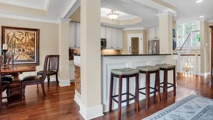 A spacious kitchen with white cabinets, a central island with stools, and a dining area with a wooden table and chairs. - 1112 Harbour South Club Villa at The Sea Pines Resort (Hilton Head Island)
