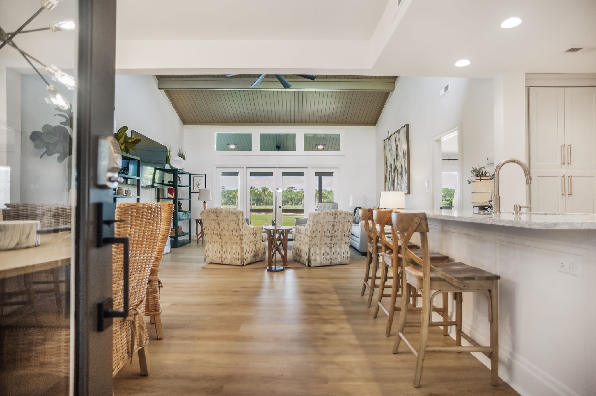 A spacious kitchen with a high ceiling, wooden flooring, and a large window offering a view of the outdoors.