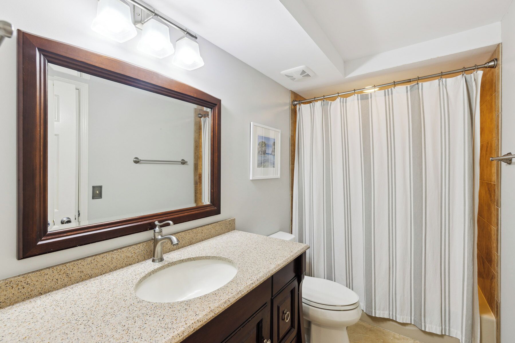 Une salle de bain avec un grand miroir, un lavabo, des toilettes et un rideau de douche.