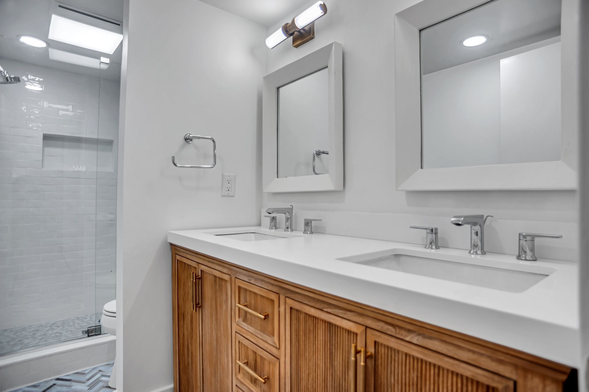 A modern bathroom with two sinks, wooden cabinets, a mirror, and a shower area.