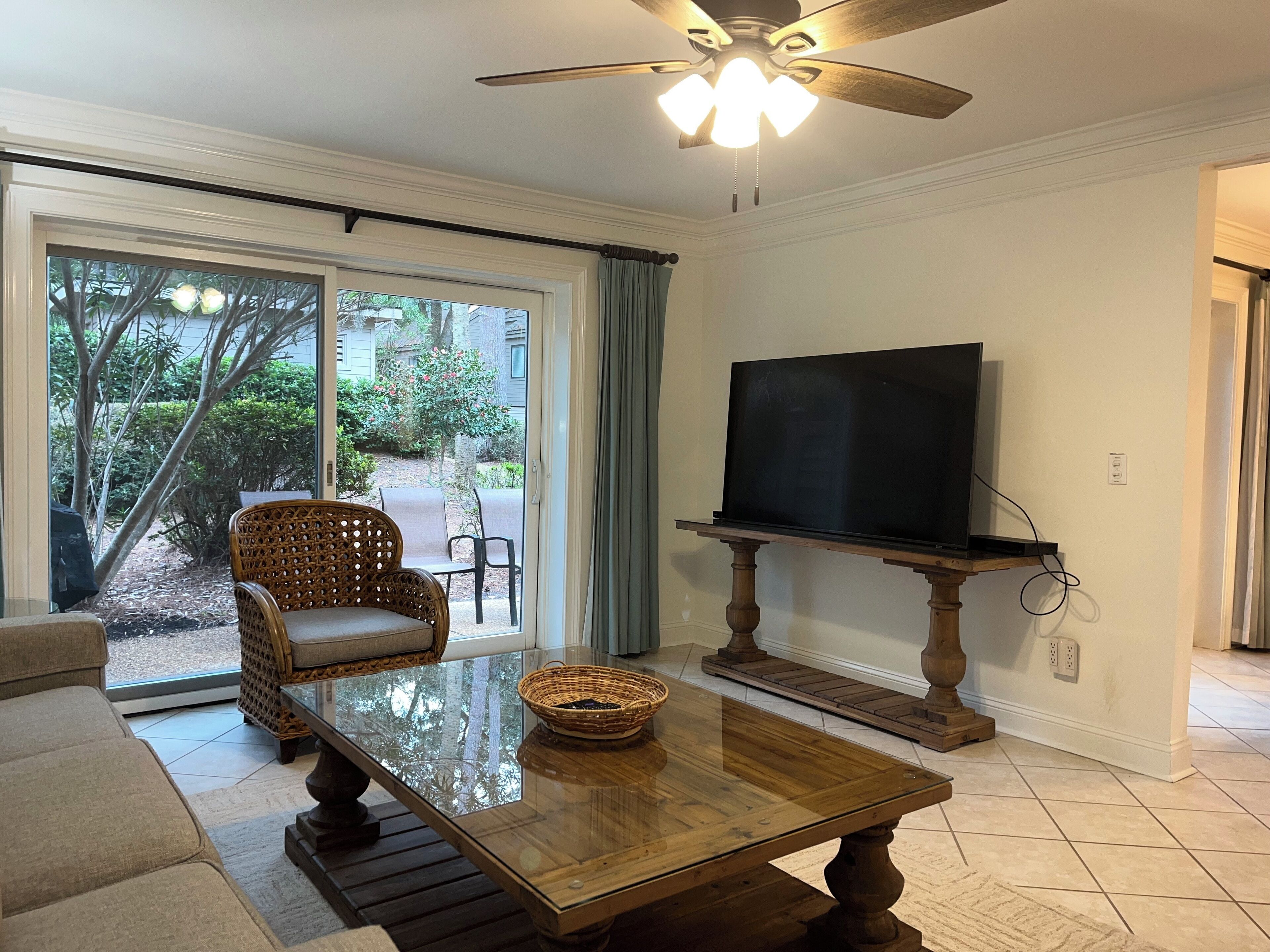A living room with a TV on a stand, a sofa, a coffee table, and a ceiling fan.