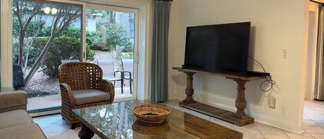 Una sala de estar con televisor sobre un mueble bajo, sofá, mesa de centro y ventilador de techo.