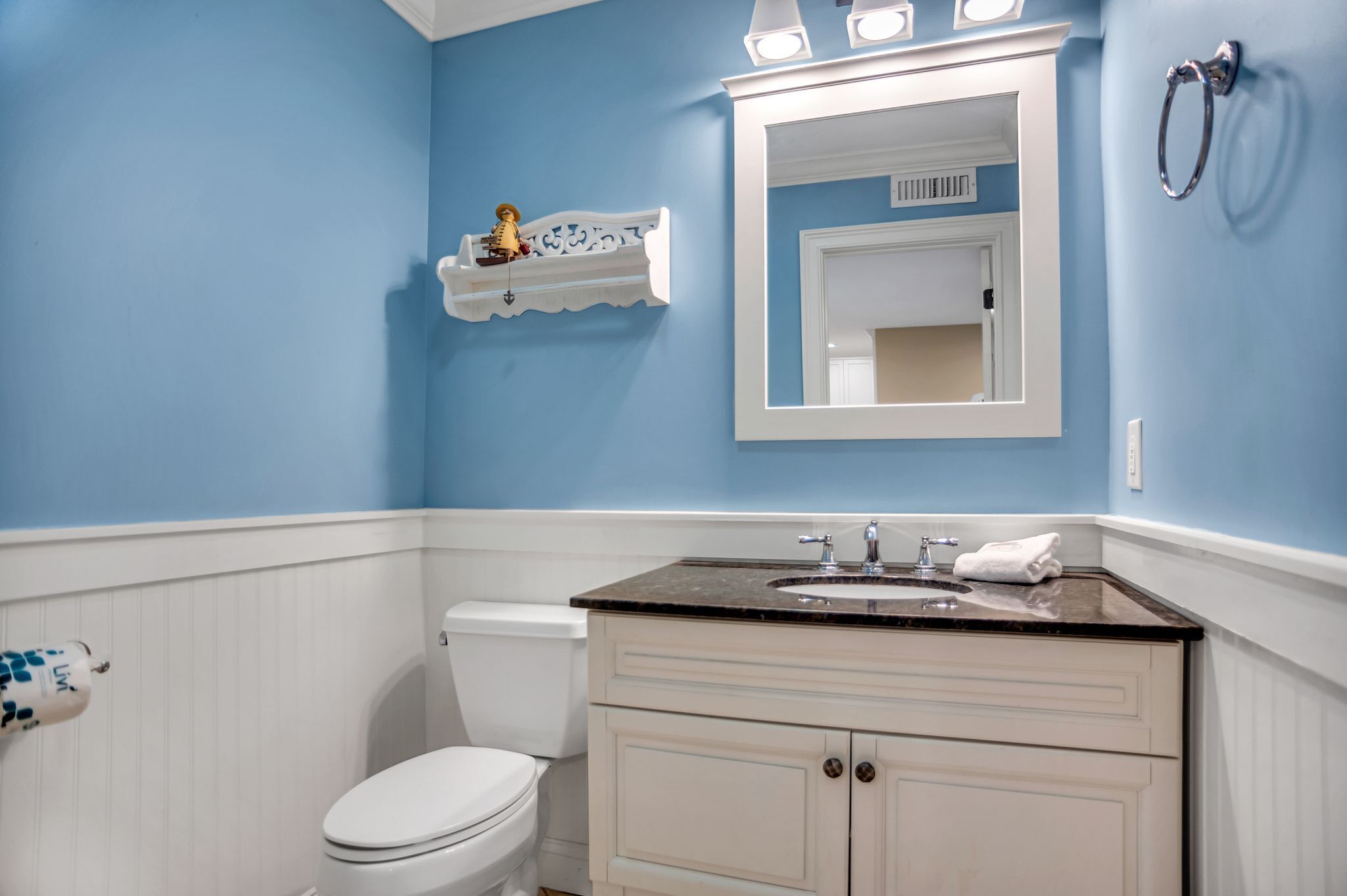 Un baño con inodoro blanco, lavamanos con espejo y pared azul.