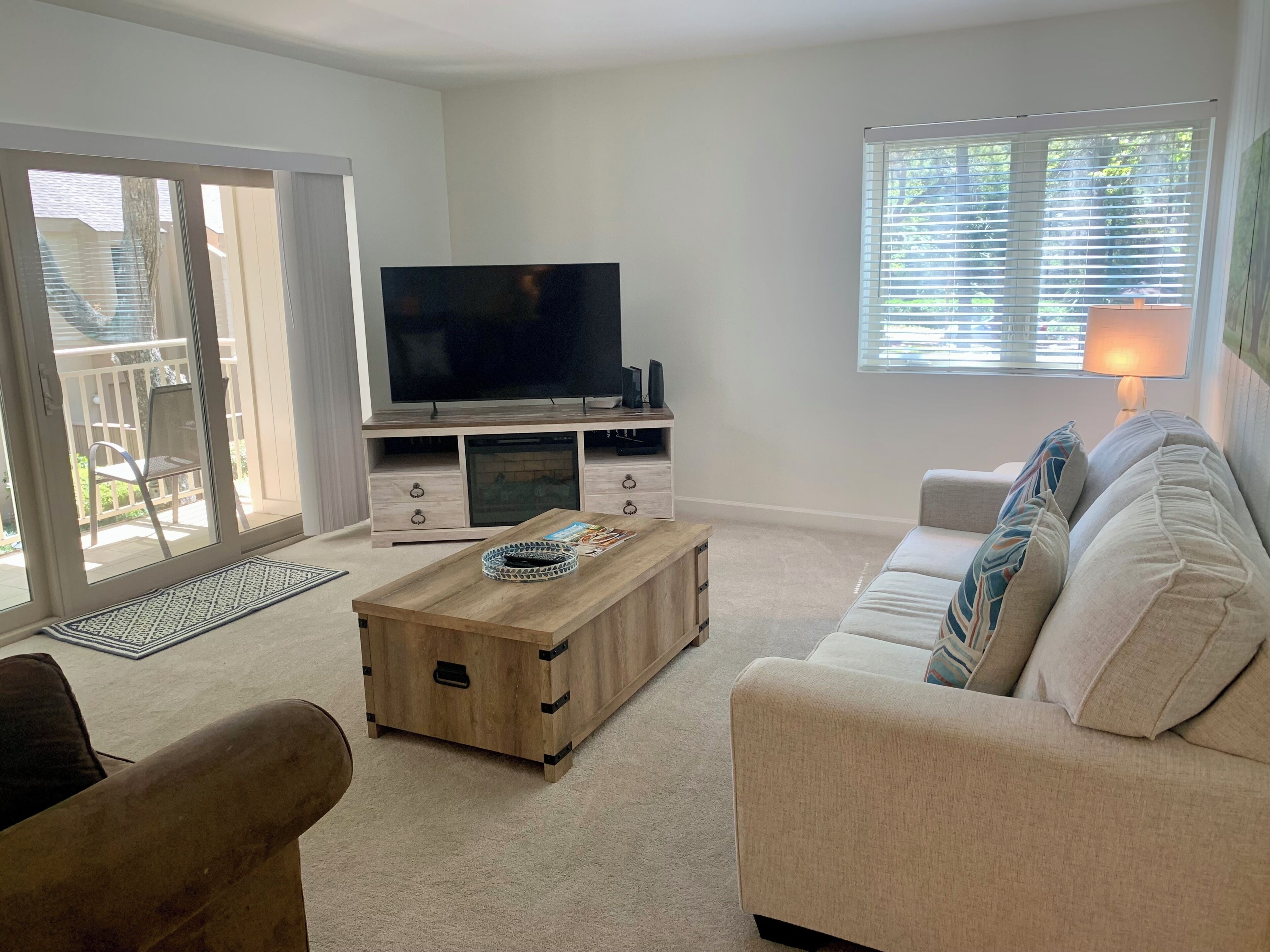 A living room with a TV, sofa, coffee table, and a sliding glass door leading to an outdoor area.