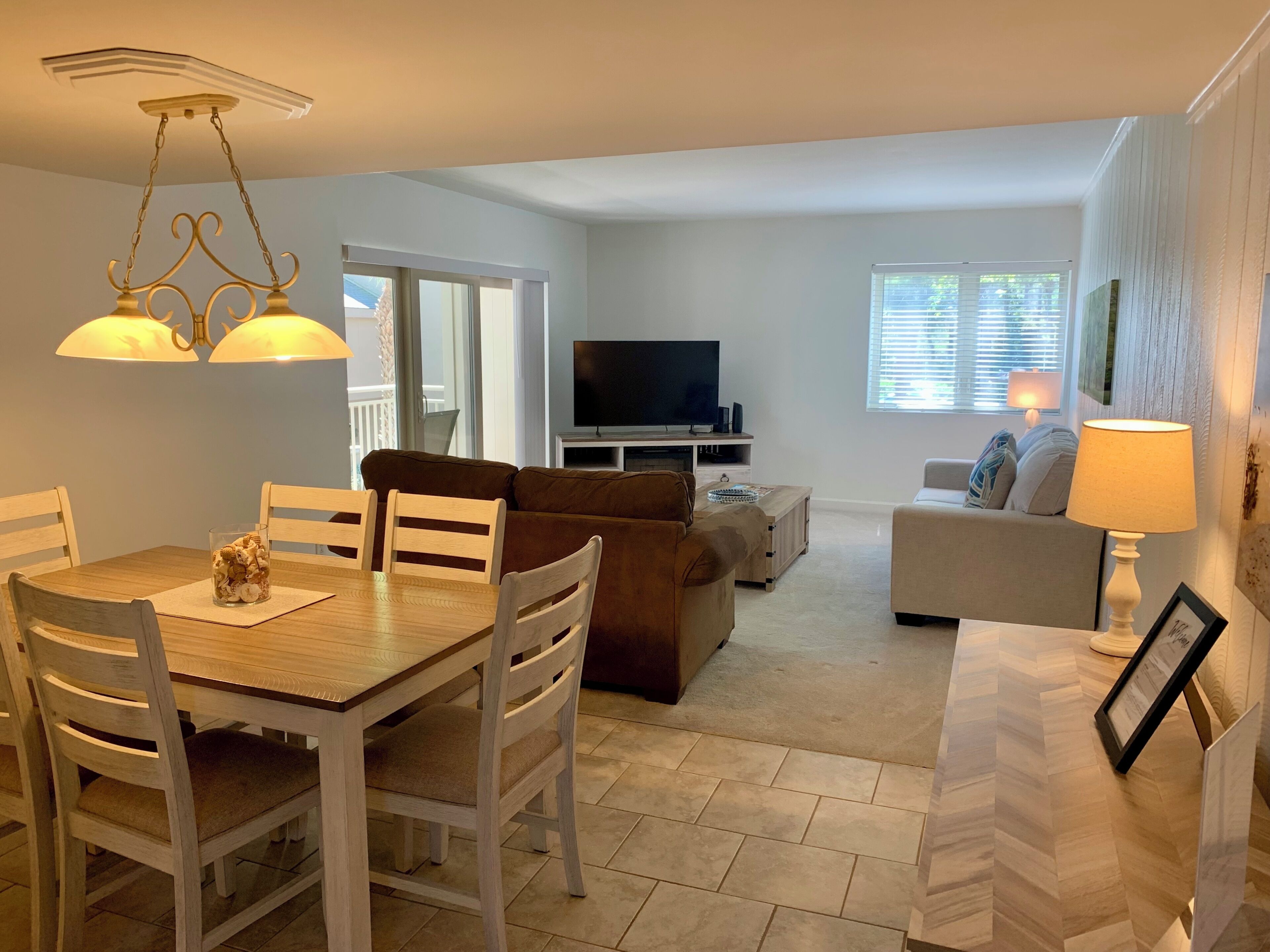 A dining area with a wooden table and chairs, a sofa, a TV stand, and a lamp.