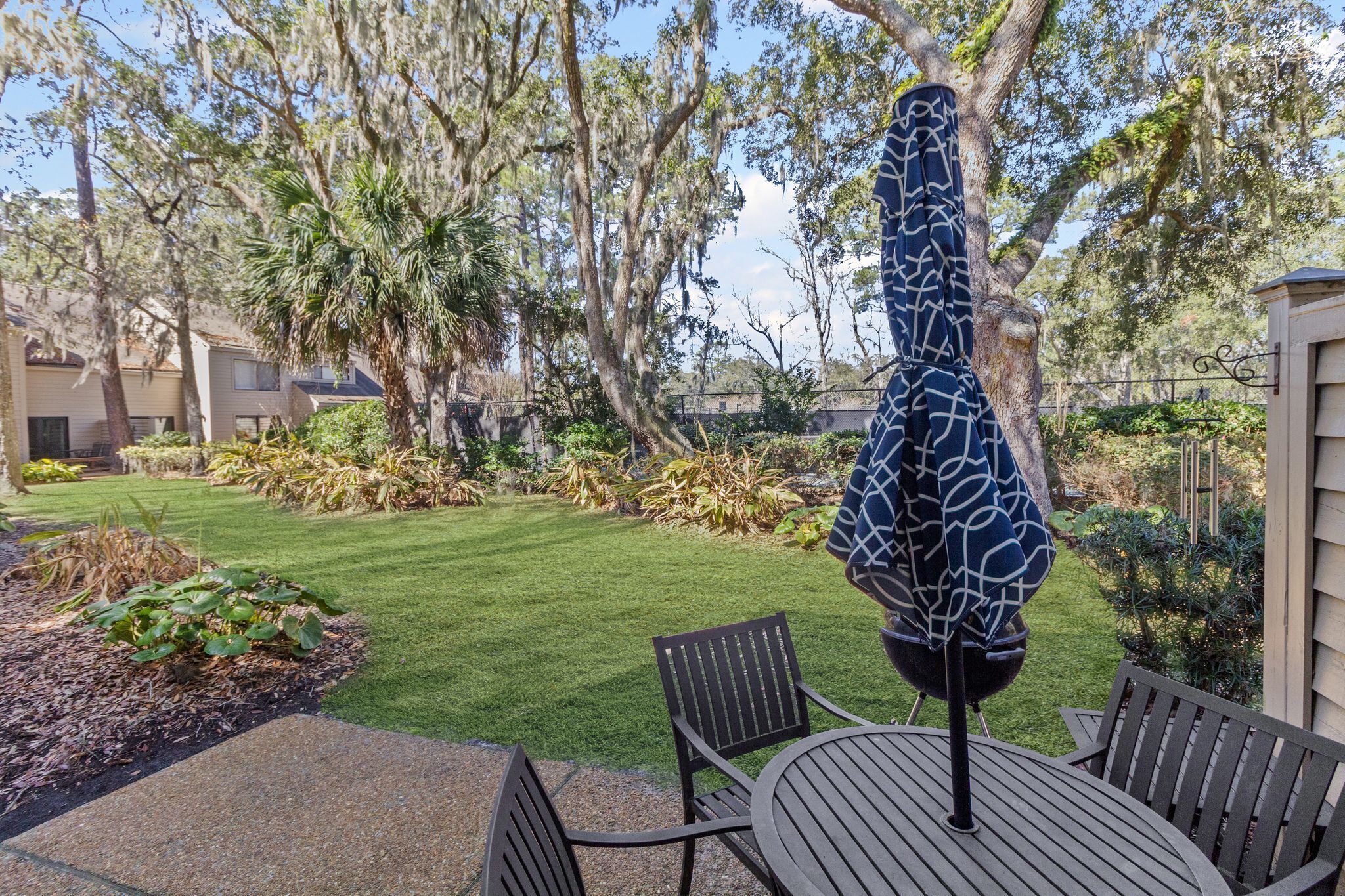 A patio area with a table and chairs, surrounded by a well-maintained lawn and trees.