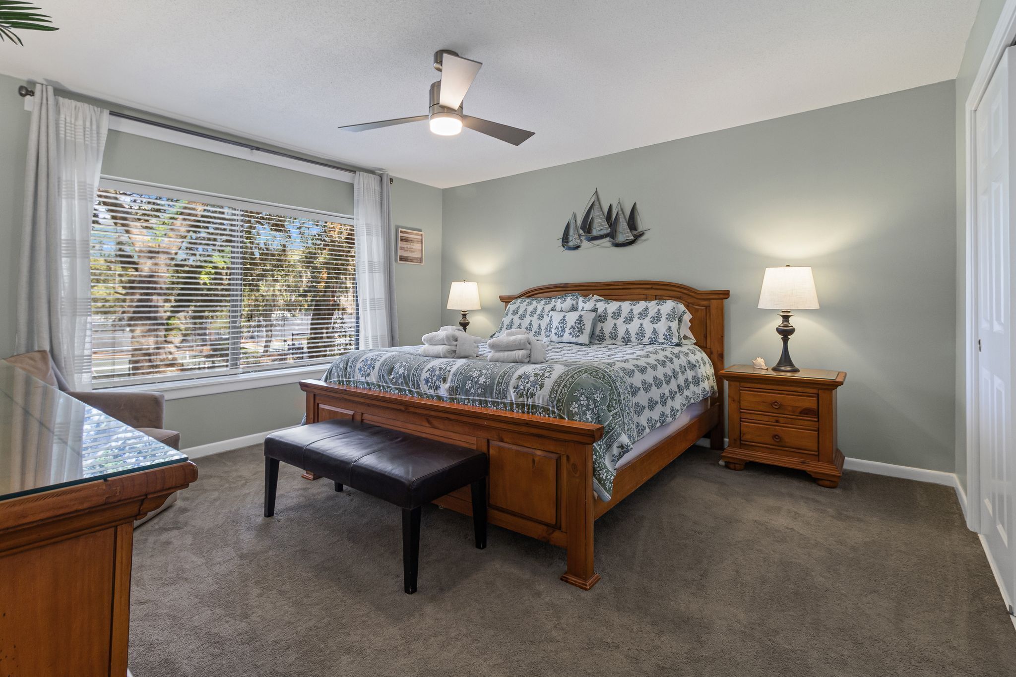 A bedroom with a bed, a bench, a desk, and a ceiling fan.