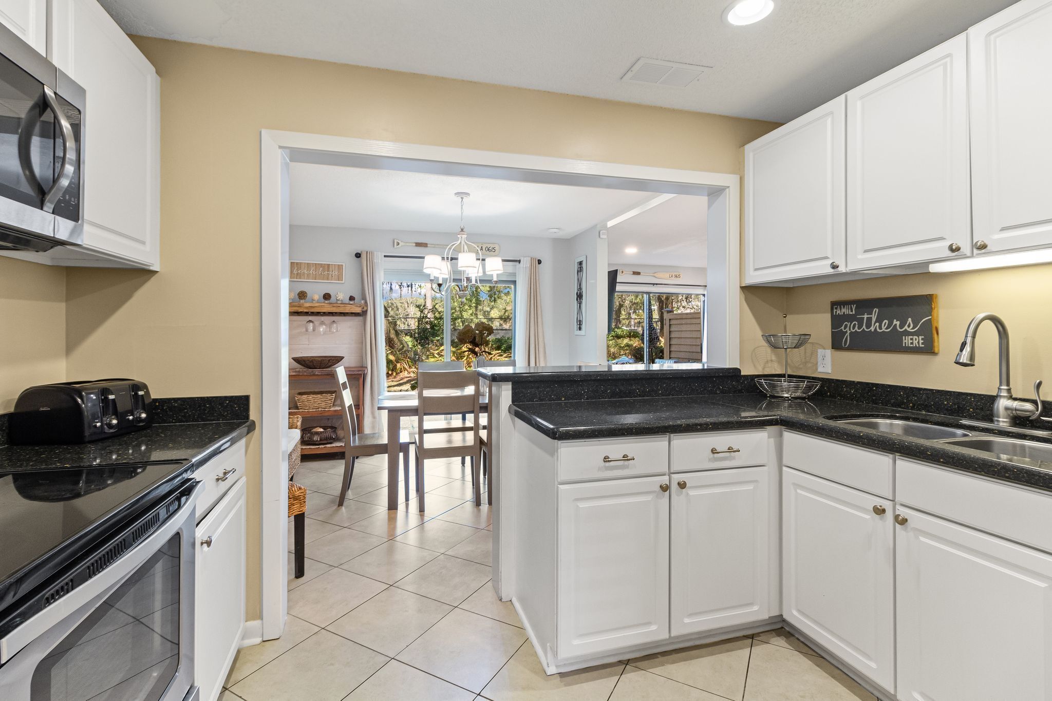 A kitchen with white cabinets, a black countertop, and a stainless steel sink.